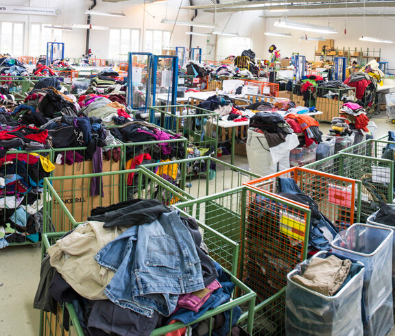 Eine Lagerhalle vom carla Sortierwerk. Es sind unzählige Schiebewägen mit Kleidung befüllt. Diese stehen verteilt in der ganzen großen Halle. 