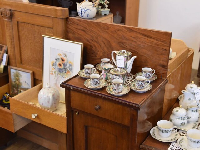 Ein Bereich des carla Shops in der Steiermark mit einer Auswahl an Vintage-Geschirr, Teetassen und Kannen, dekorativ arrangiert auf einem Holzmöbel.