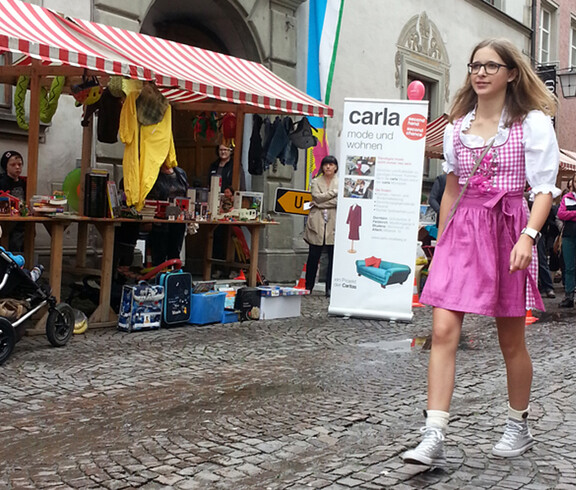 carla stellte anlässlich des Reuse Days zwei Stände in der feldkircher Innenstadt vor auf. Eine Fußgängerin mit pinkem Dirndl spaziert vorbei. 