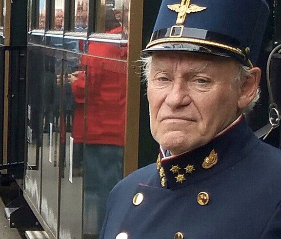 Ein alter, unsympatisch im Gesichtsausdruck wirkender Eisenbahner mit blauer Uniform mit Manschettenköpfen. 