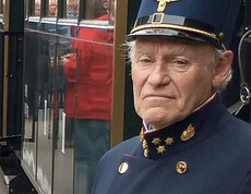 Ein alter, unsympatisch im Gesichtsausdruck wirkender Eisenbahner mit blauer Uniform mit Manschettenköpfen. 