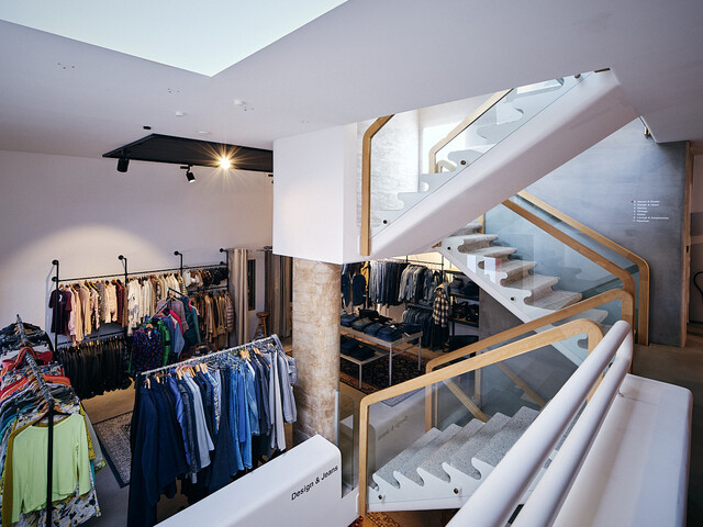 Helle Verkaufsfläche im Carla Store Vorarlberg mit moderner Treppe und Kleiderständern voller Secondhand-Kleidung.