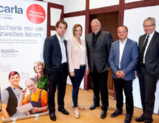 Fünf Menschen versammeln sich neben einem Carla Stehplakat für ein Gruppenfoto.