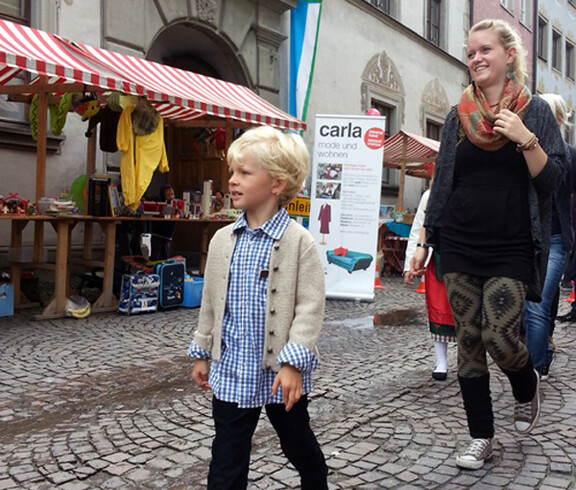 Sowohl eine junge Erwachsene als auch Kinder in Tracht gehen durch die feldkircher Innenstadt um ihre modische Kleidung zu präsentieren. 
