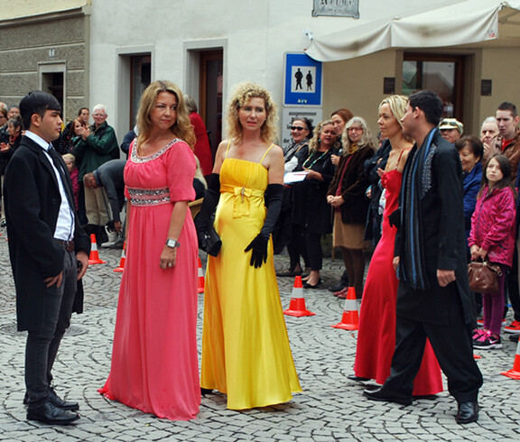 Frauen und Männer im mittleren Alter sind auch bei der carla Modeschau beim Reuse Day in der feldkircher Innenstadt dabei. Die Damen tragen ein langes rotes bzw. gelbes Kleid, die Herren einen schwarzen Anzug. 