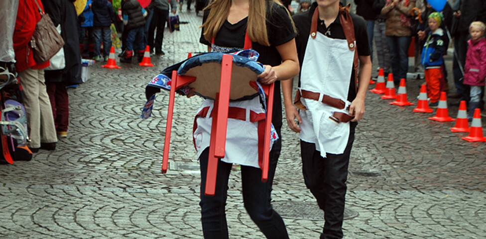 Eine junge Erwachsene und ein junger Erwachsener tragen schwarze Kleidung mit einer weißen Schürtze. Sie präsentieren diese Kreation in der feldkircher Innnenstadt Passanten am carla Reuse Day. 