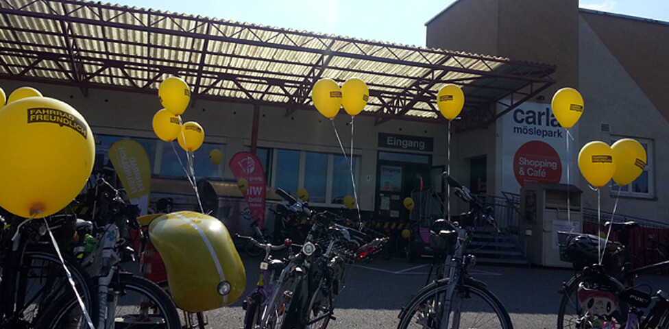 Beim carla Möslepark in Altach stehen etliche Fahrräder, an denen mit einer Schnur ein gelber Luftballon befestigt wurde. 