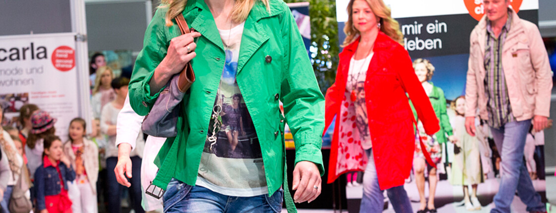 carla Modeschau: Models unterschiedlichen Alters laufen schick gestylt über den weißen Laufsteg. Dabei tragen die Teilnehmerinnen unterschiedliche Farben wie grün, rot und beige. 