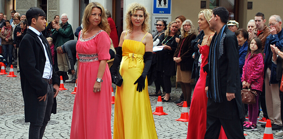 Frauen und Männer im mittleren Alter sind auch bei der carla Modeschau beim Reuse Day in der feldkircher Innenstadt dabei. Die Damen tragen ein langes rotes bzw. gelbes Kleid, die Herren einen schwarzen Anzug. 